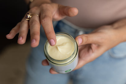 A person who is holding the shea + cocoa body butter and displaying the texture of the cream